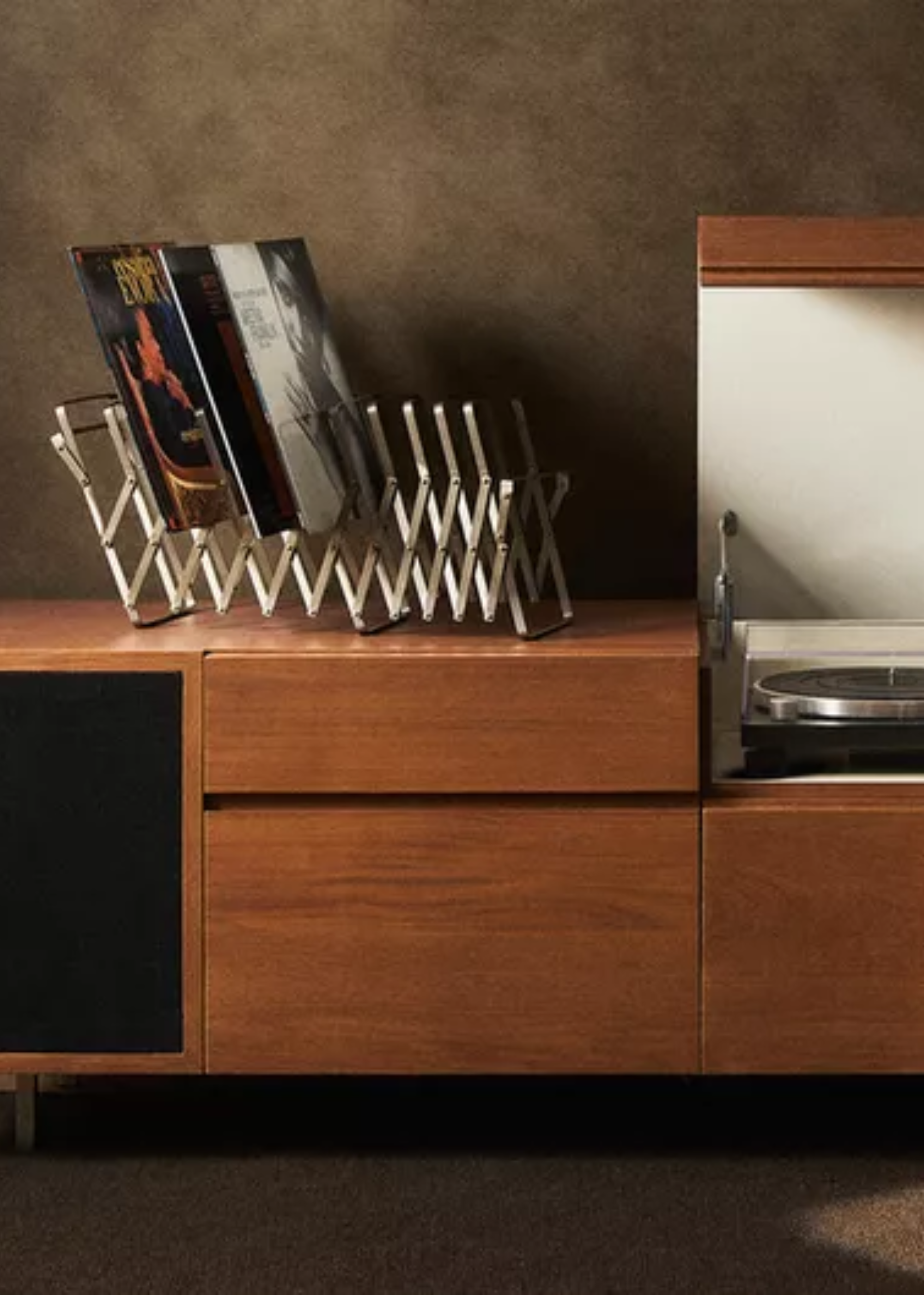 A close-up of a record bar made from wood with compartments for speakers, an extendable rack on top of the console with records and an open compartment with a turntable