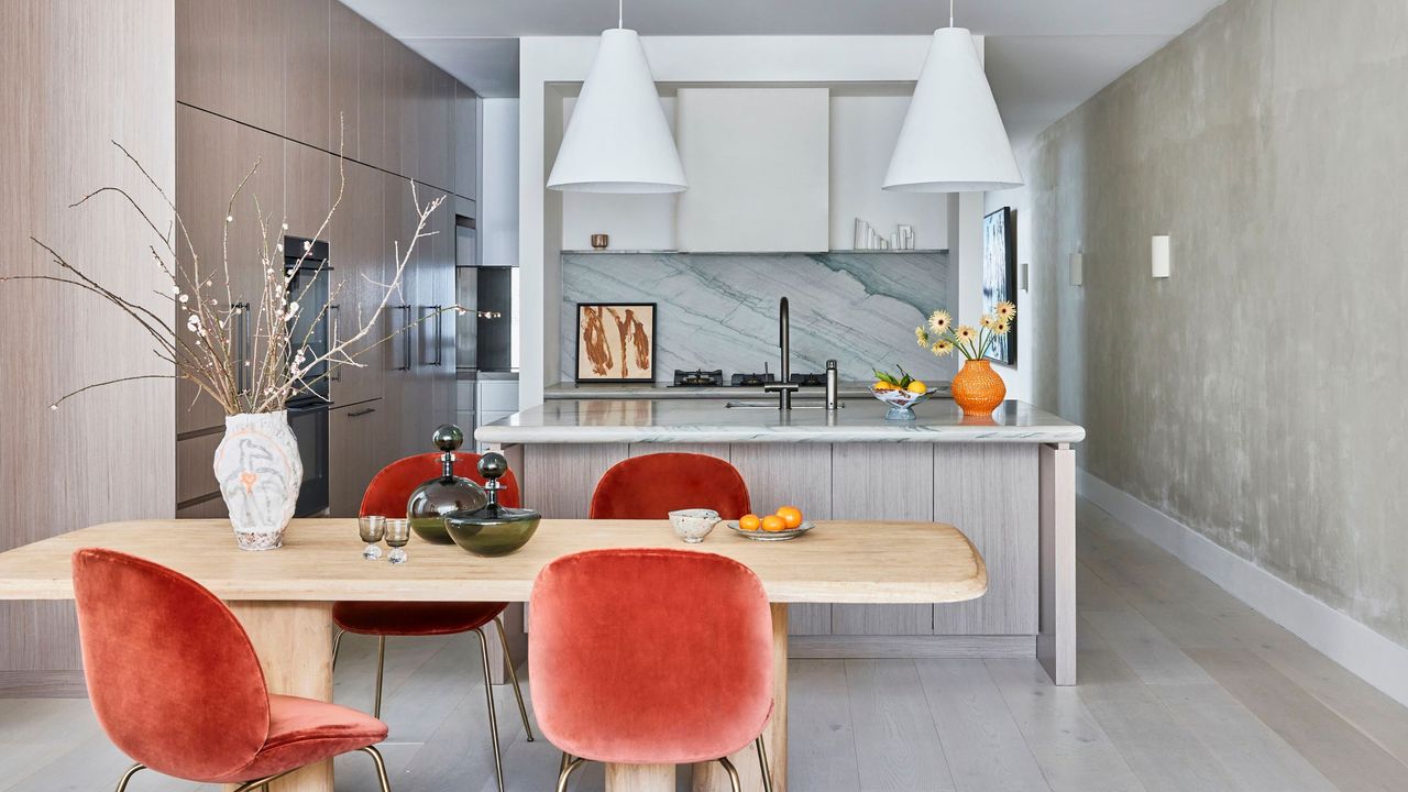 colorful kitchen with light blue marble backsplash, venetian plaster walls, two pendant lights over the island, and a timber dining table with four velvet orange dining chairs