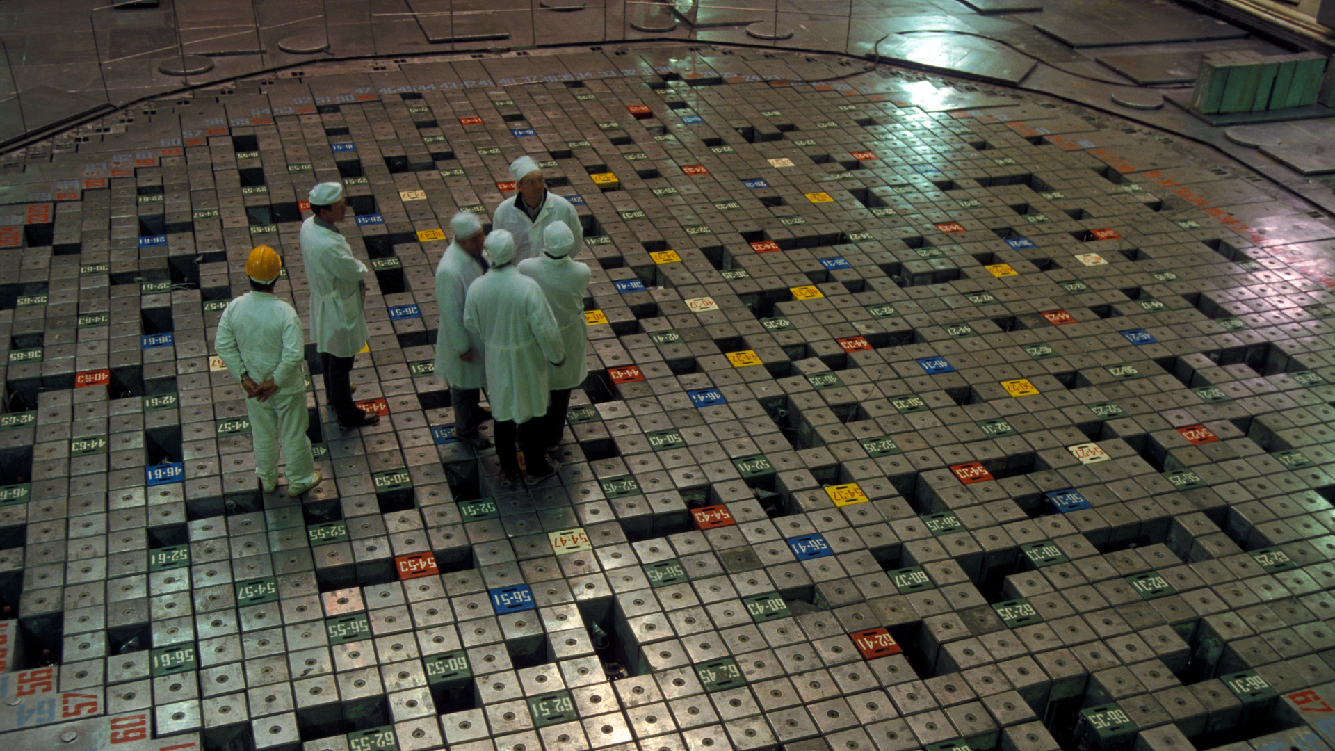 A group of people wearing white laboratory coats stand on a patterned floor in a large circular room.