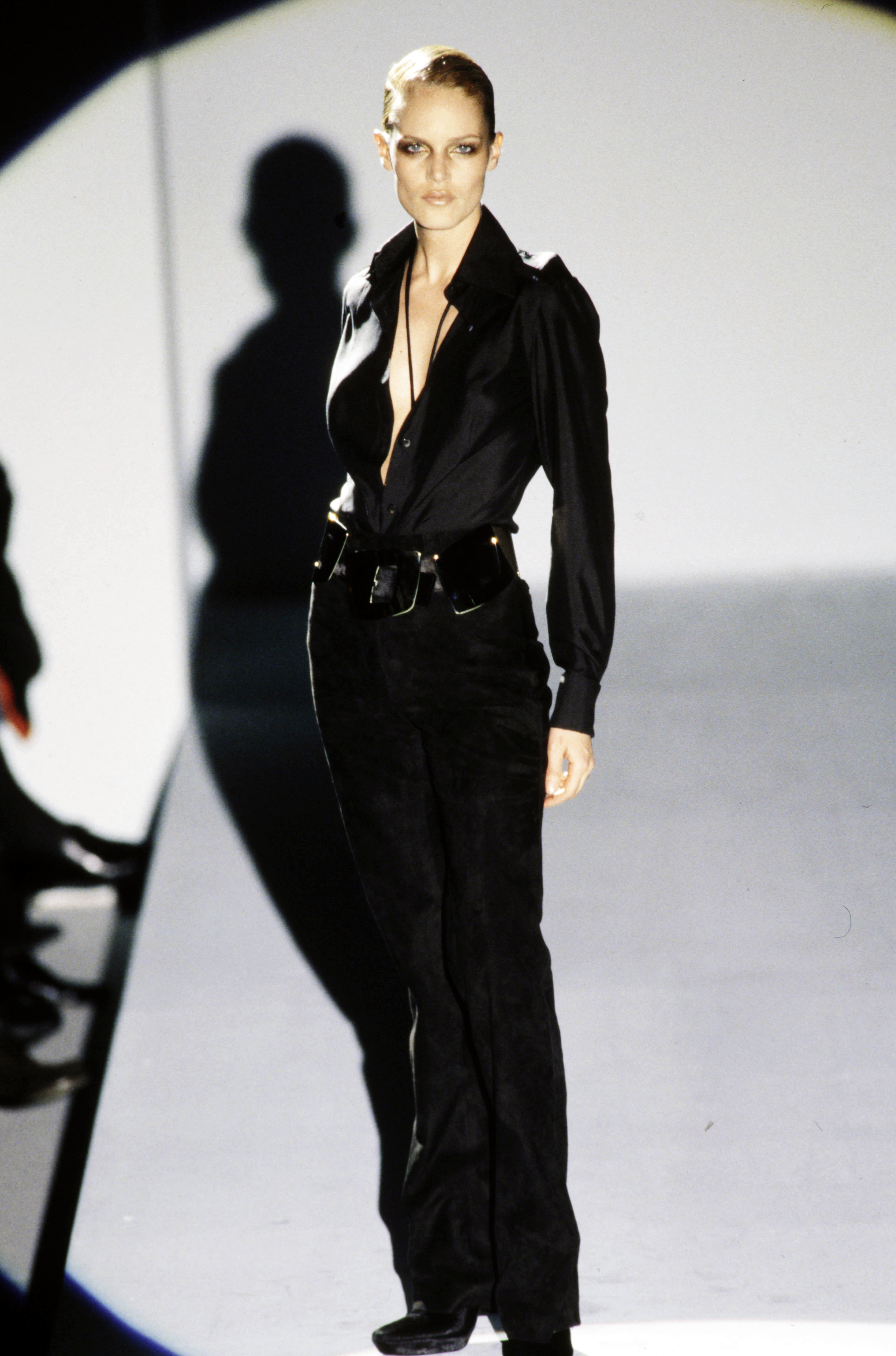 Runway model wearing a black satin shirt and black trousers.