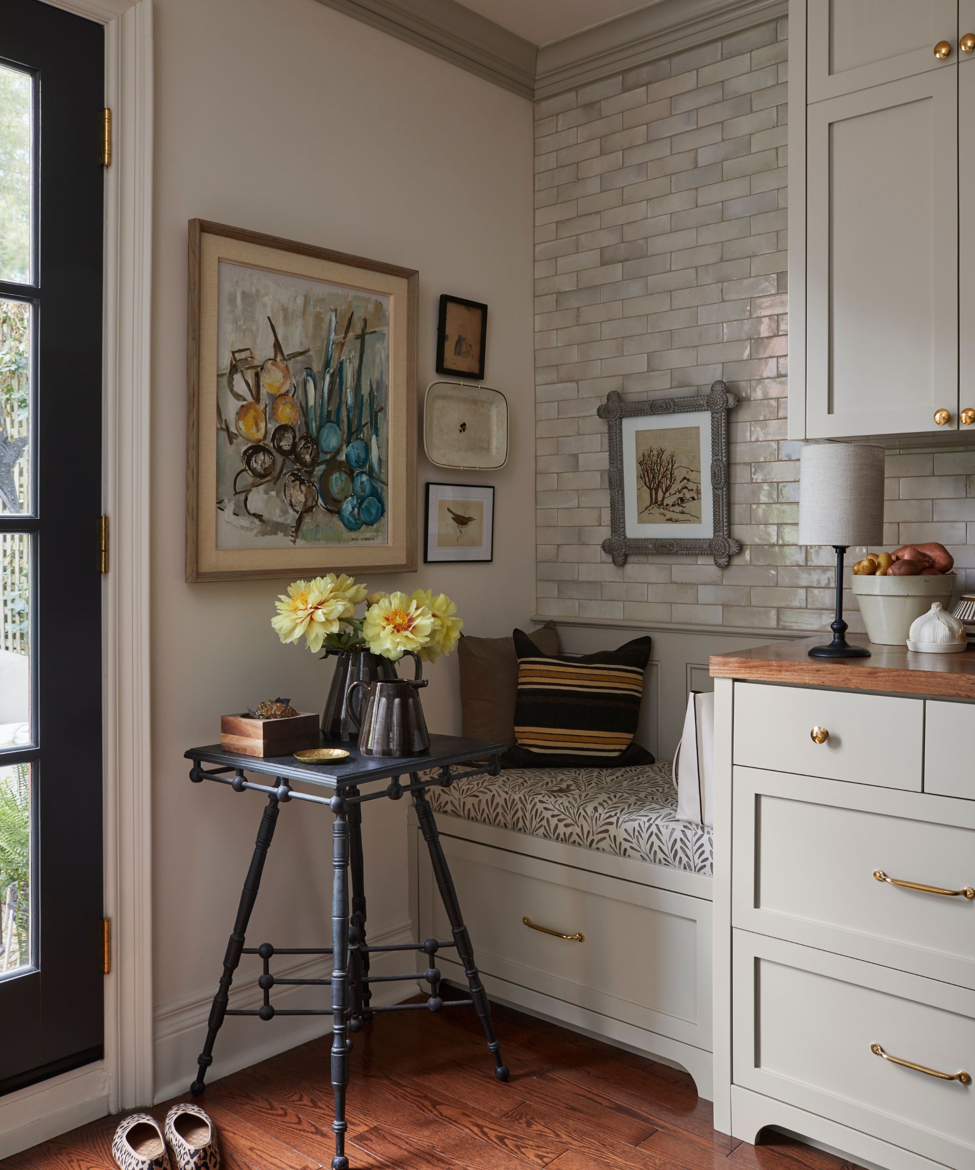 The corner of a vintage-style kitchen with a banquette topped with patterned pillows and walls covered in collected art