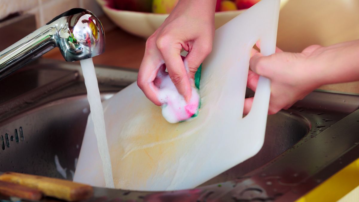 woman washing a stained cutting board in the sink