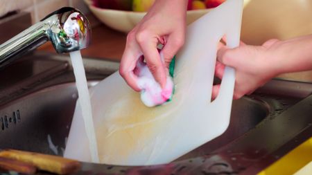 woman washing a stained cutting board in the sink