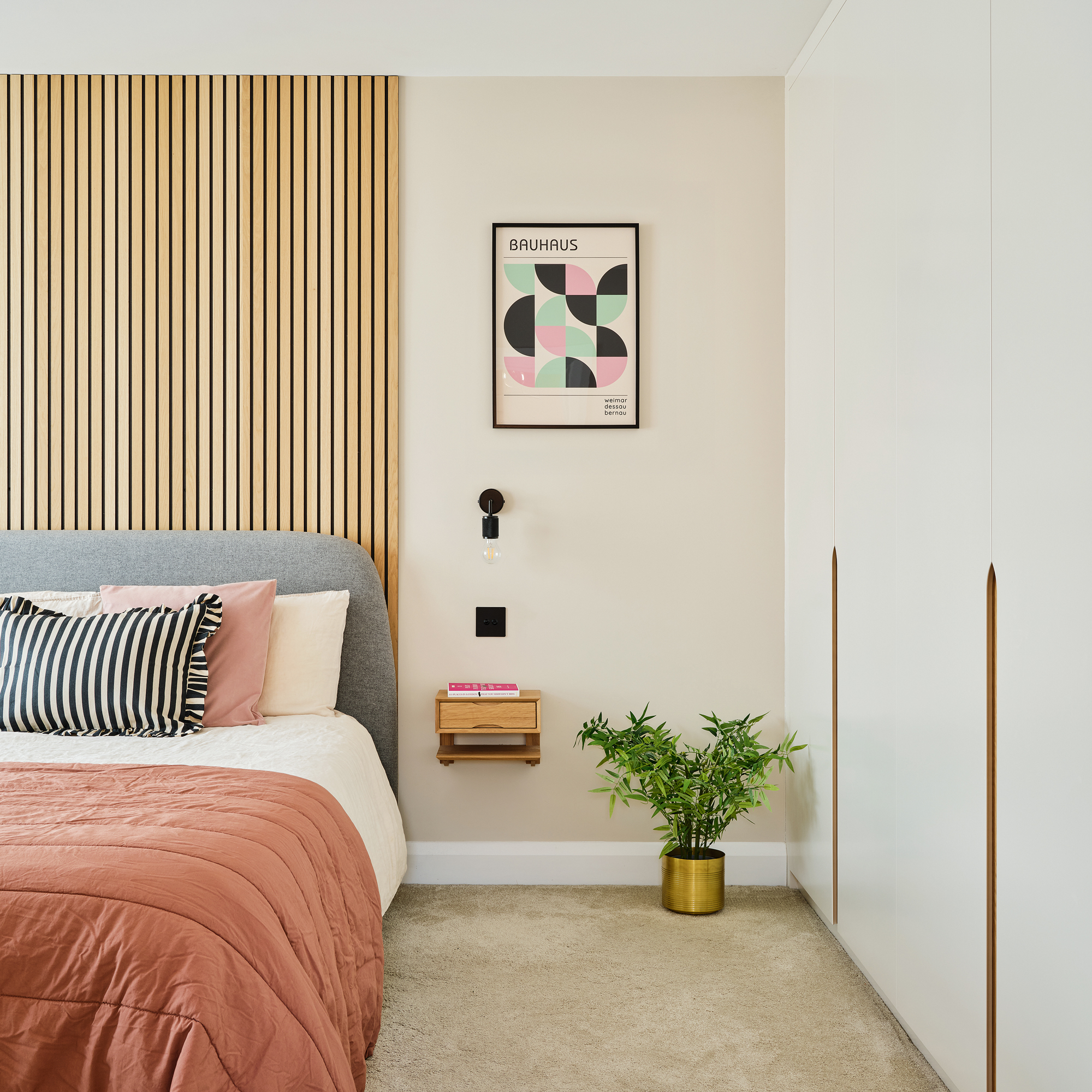 double bedroom with pale walls, pink and terracotta bedding and vertical wall panelling for a headboard