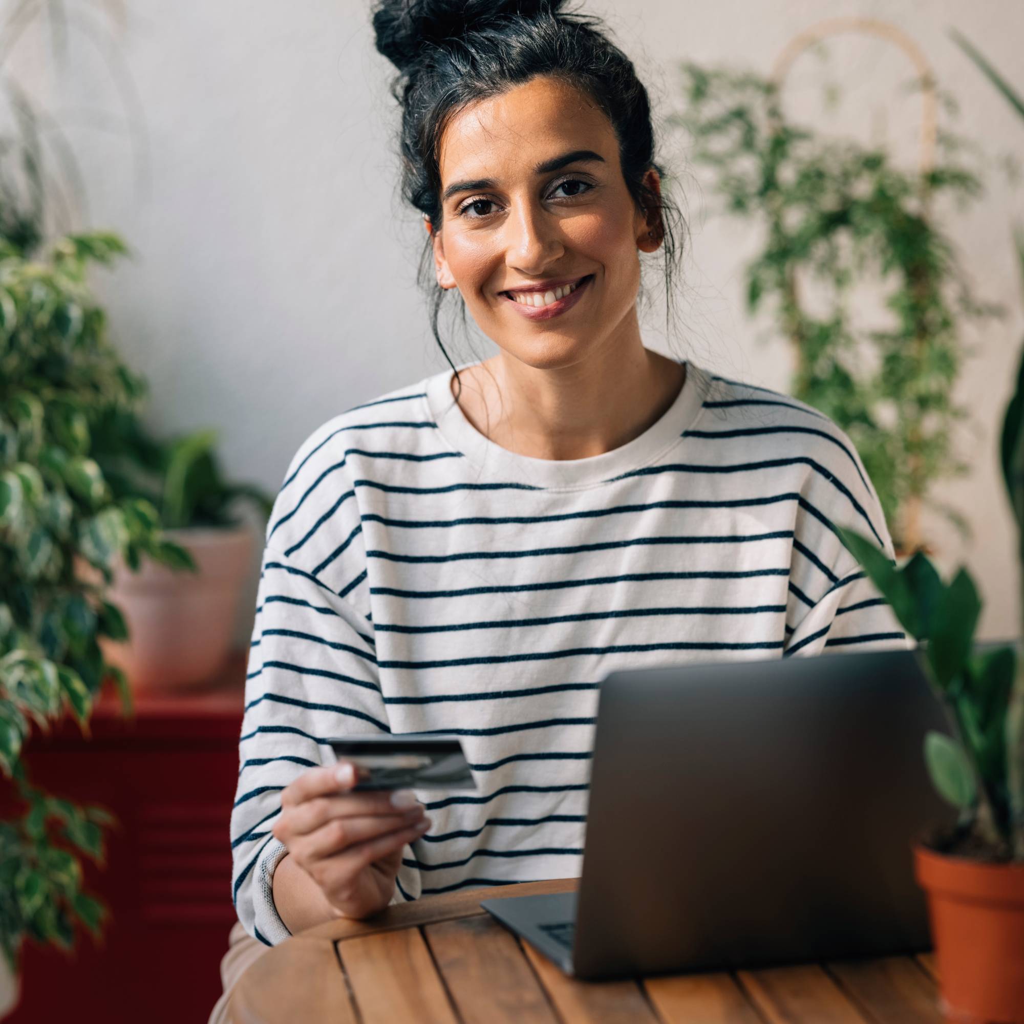 A woman at a laptop smiles holding a credit card