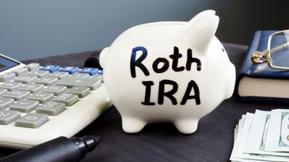 A piggy bank sitting next to a calculator has Roth IRA written on it in black marker.