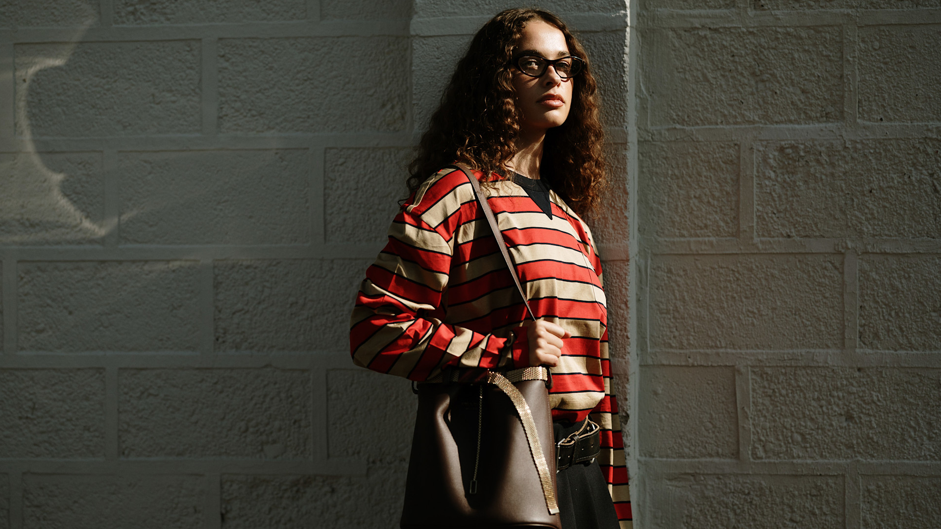 fashion week attendee wears glasses, red striped shirt, and brown handbag