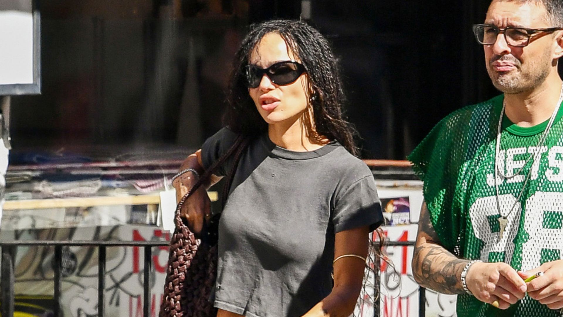An image of Zoe Kravitz wearing suede bootcut jeans with beige heels, a grey T-shirt and woven leather bag. 