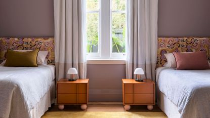 bedroom with twin beds, lavender wall, mustard yellow rug, orange side tables and curtains