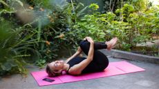 Woman lying down on yoga mat in back garden, doing stretches for tight hips