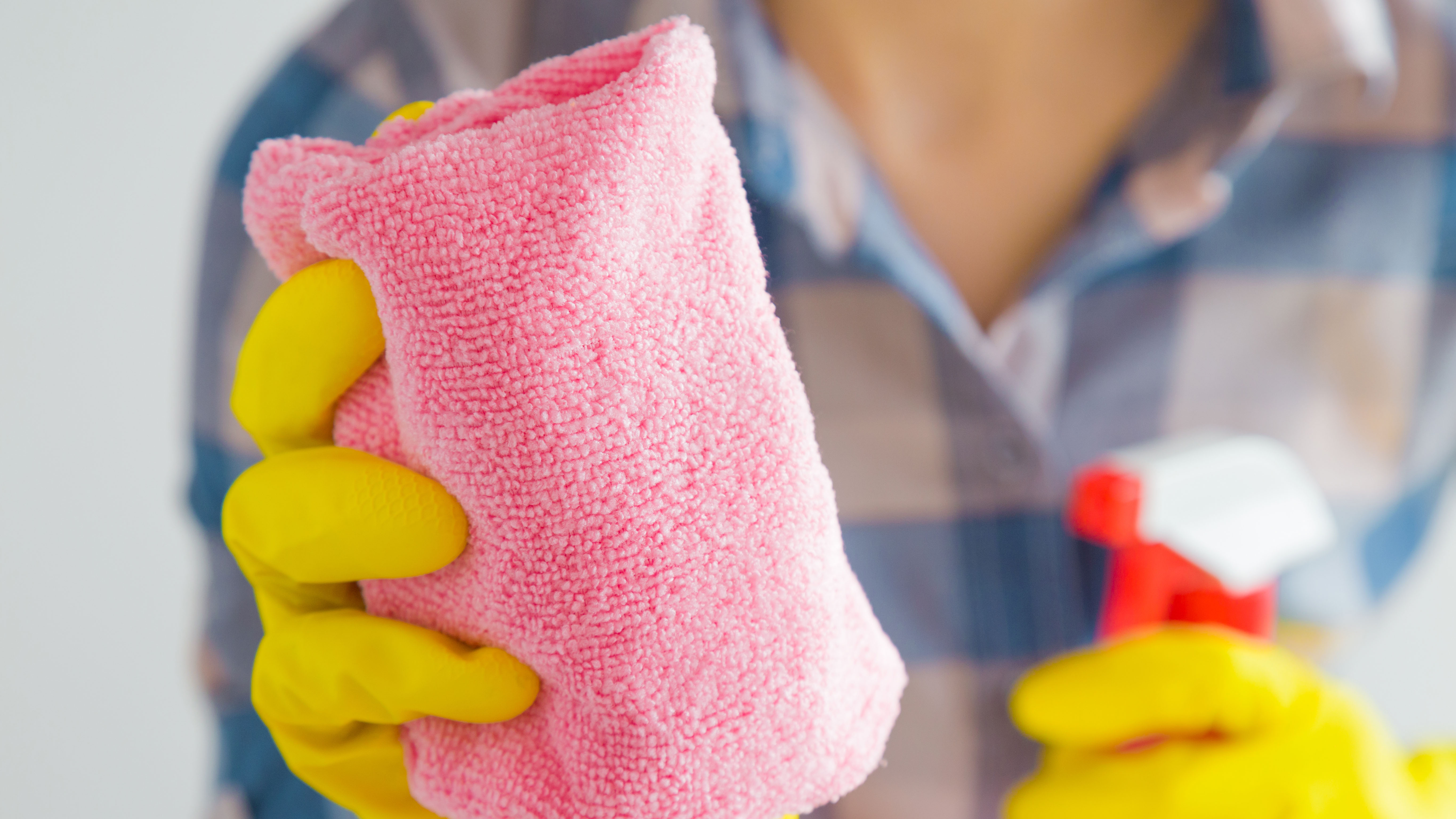 A pink microfiber cloth with a cleaning spray aimed at it held by gloved hands