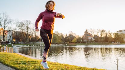 Woman looking at fitness tracker on wrist, running along park path next to lake, running 20 minutes a day