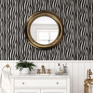 bathroom with zebra wallpaper on wall and golden round mirror