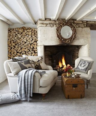 Alcove in a rustic farmhouse filled with logs and. alarge open fireplacce and comfy armchair