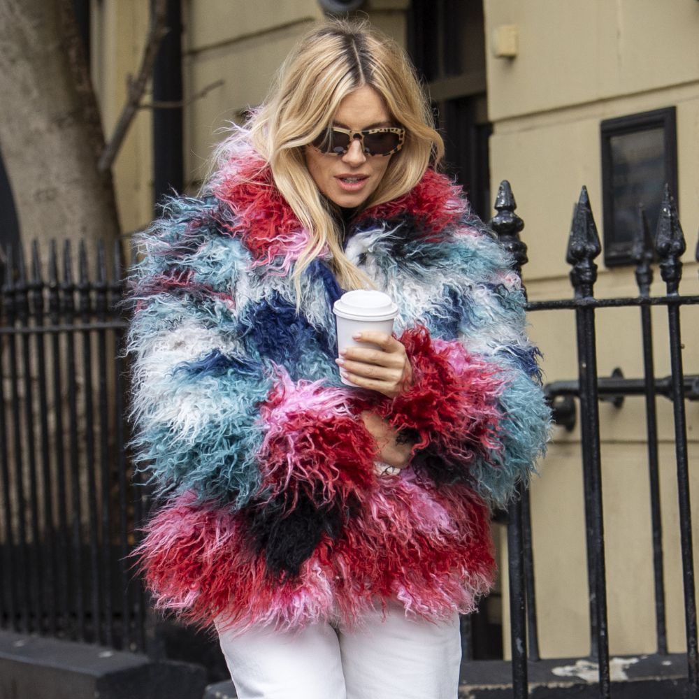 Sienna Miller walks down the street in London wearing a furry multi-coloured jacket from Desigual with white jeans and black leather ballet flats.