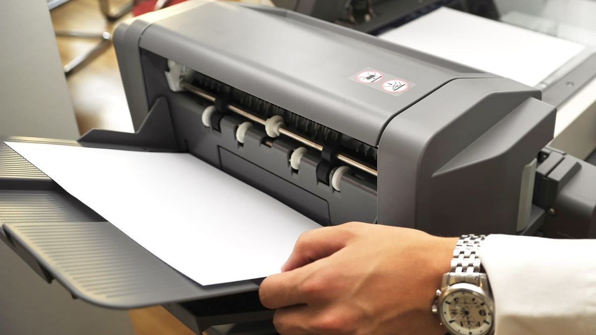 Man wearing a shirt and watch loading paper into a printer.