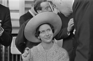 Princess Margaret wearing a giant hat and smiling while looking to the side