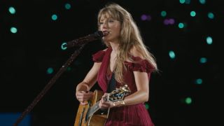 Taylor Swift playing her guitar and singing into a microphone during the Eras Tour.