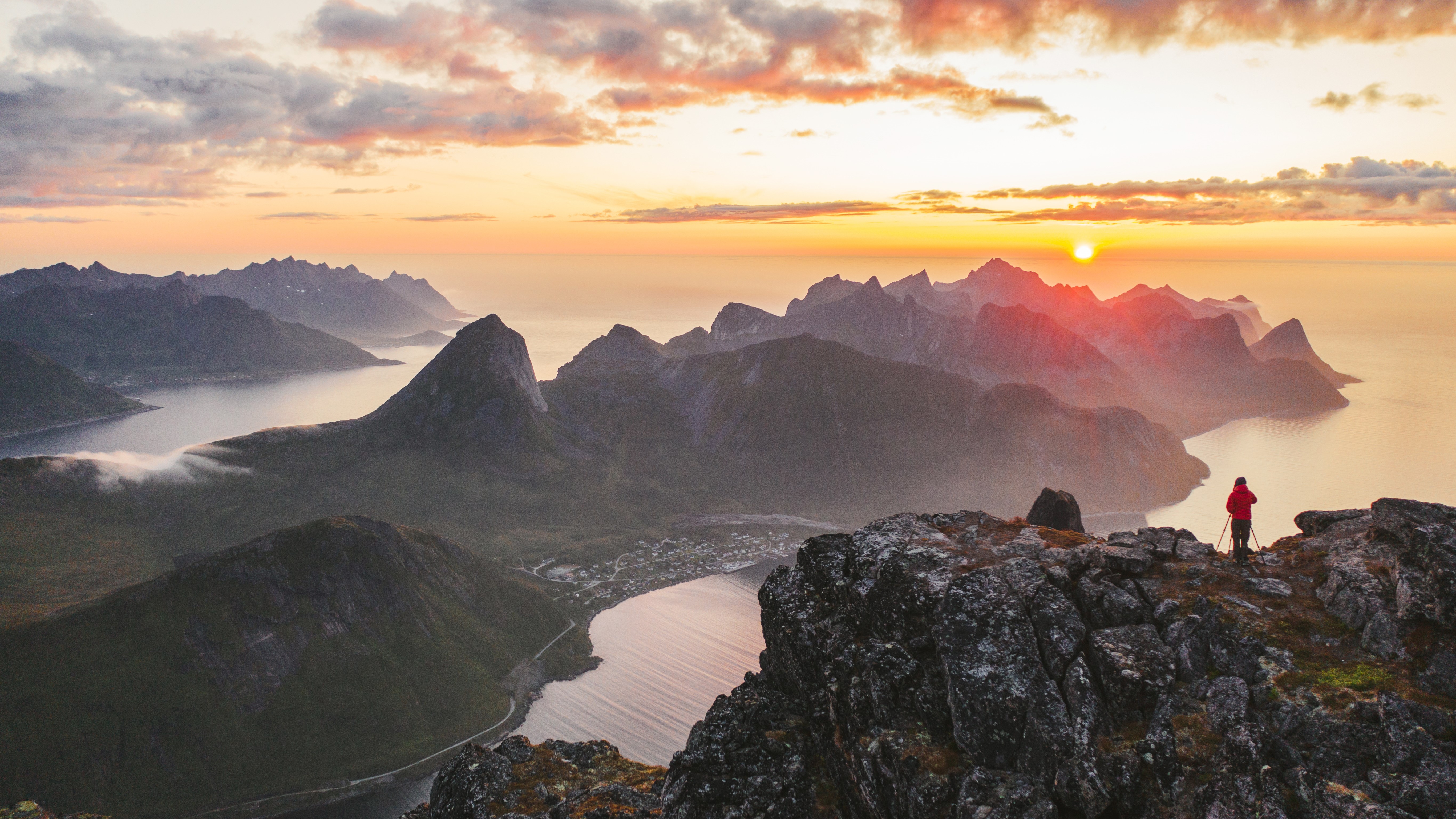 Aerial view of man wearing a red coat standing on mountain peak on Senja island