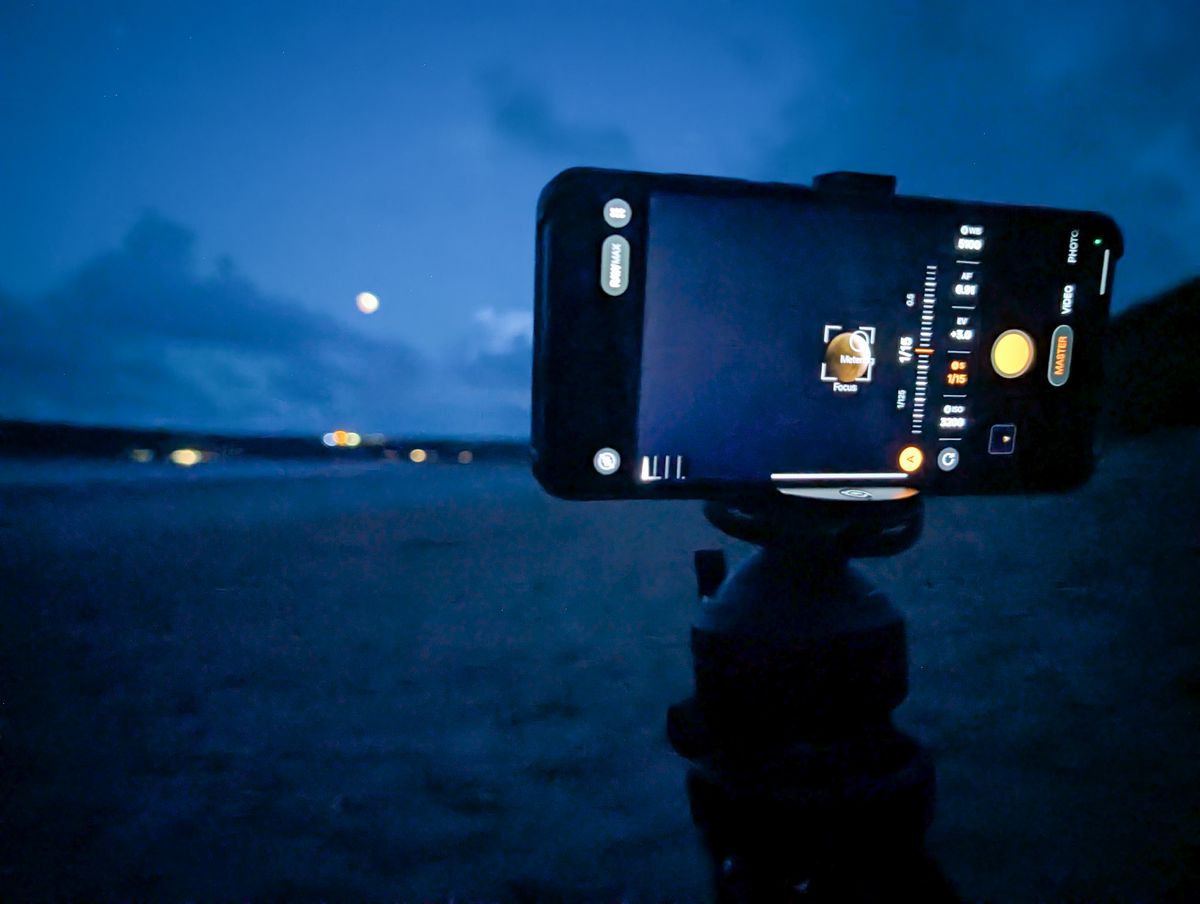 Oppo Find X9 Ultra phone with teleconverter lens mounted to a tripod on a beach at night during the 2026 lunar eclipse