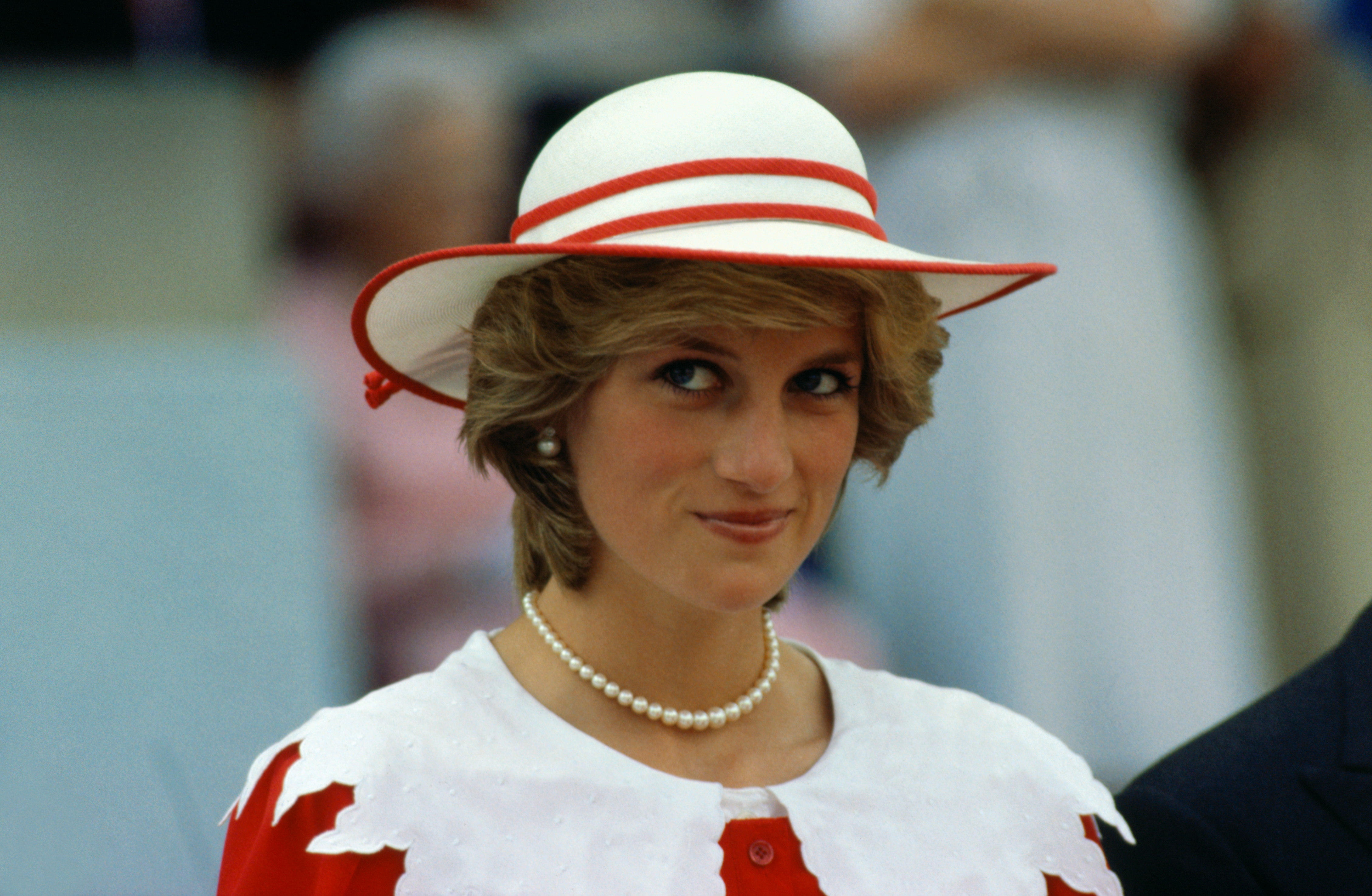 Princess Diana wearing a white hat with red trim and a matching dress and smiling