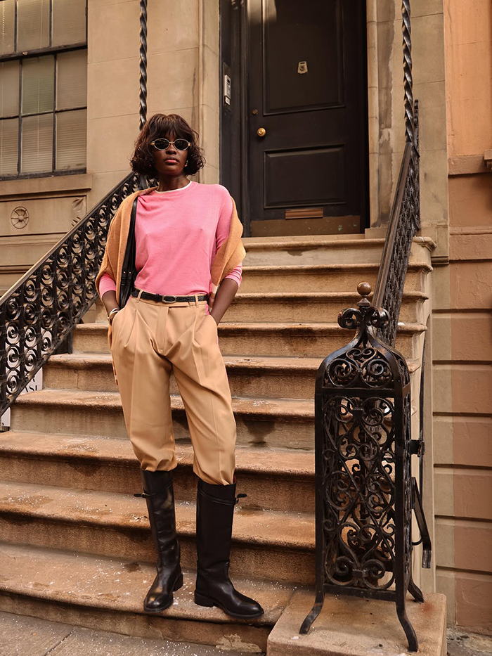 Amy Lefevre wearing a pink sweater, tan trousers, and tall black boots.