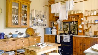 a freestanding kitchen full of wooden furniture, including a wooden cabinet fixed to the wall, a chest of drawers to the left, a butcher's block in the middle, and an aga inside a fitted wooden kitchen unit, with tea towels hanging from a ceiling rail above