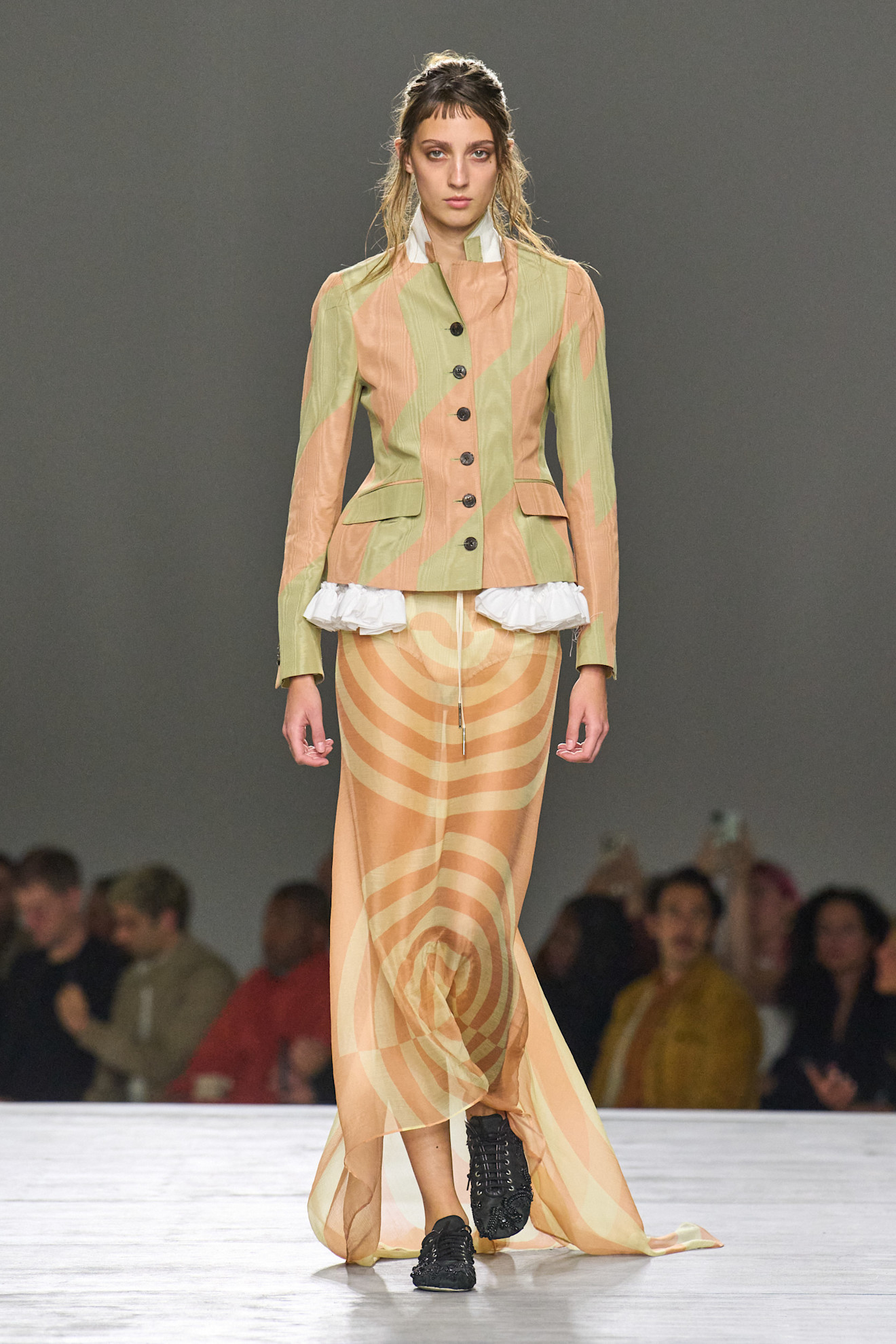 A model at the spring/summer 2026 Dries Van Noten show wearing a sculpted blazer with a ruffle underlay and a sheer, patterned skirt.