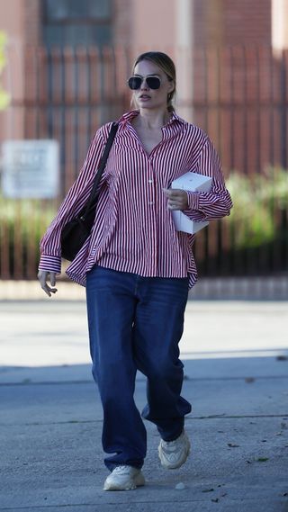 Margot Robbie wearing an oversized red and white button down with baggy blue jeans and dad sneakers