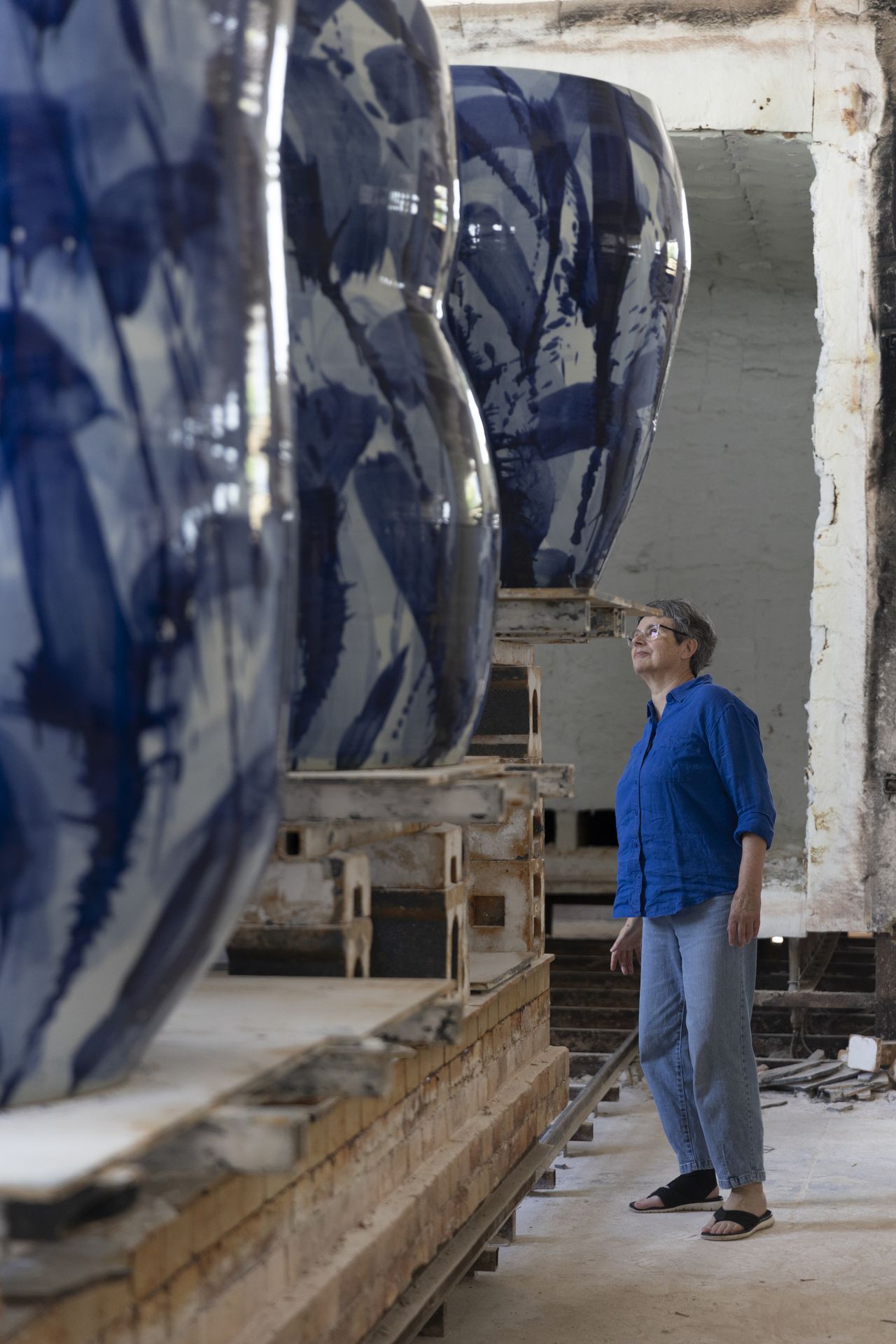 Felicity Aylieff, dressed in denim and a blue top, works and observes her large-scale porcelain vases.