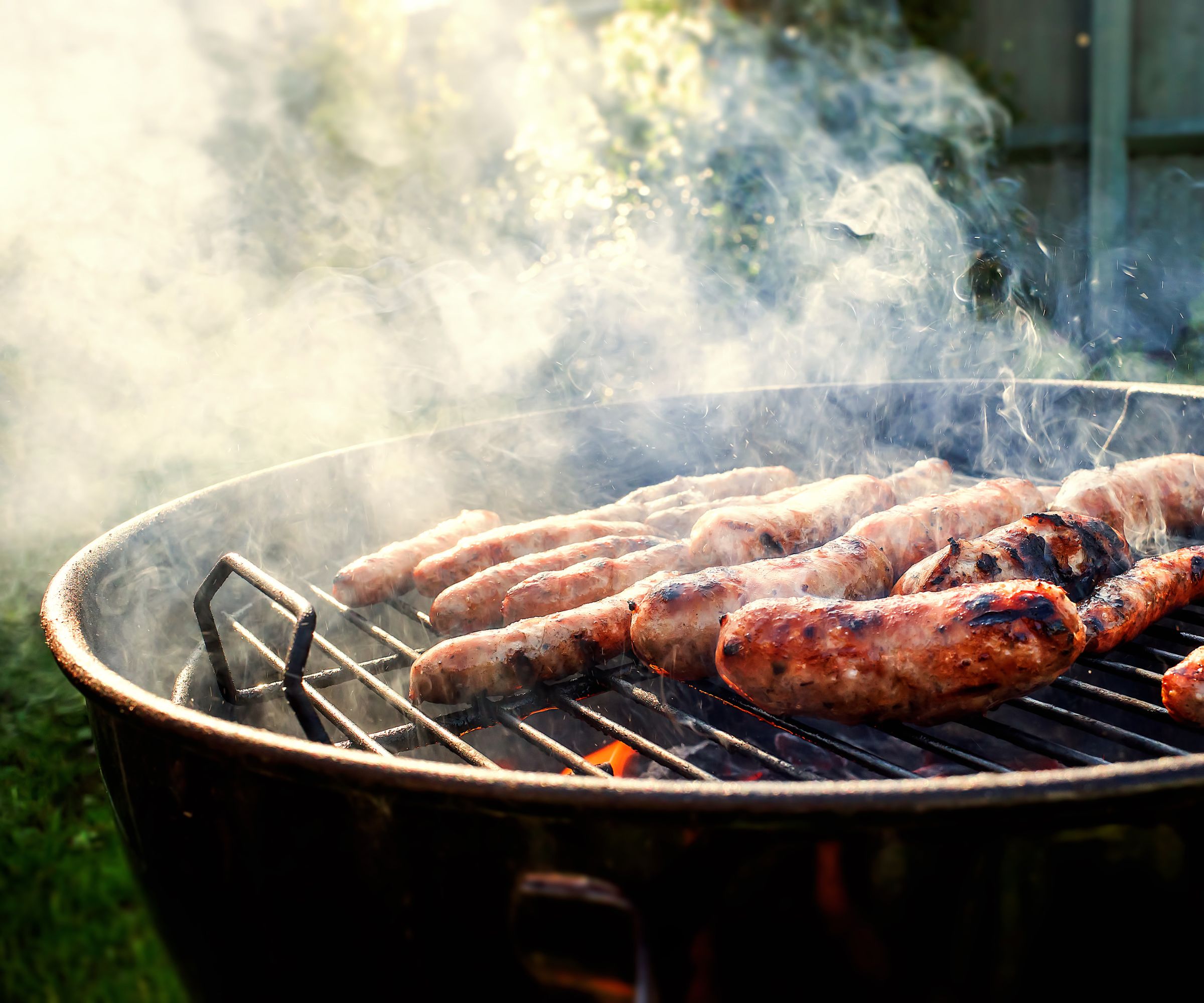 A close up of grilling sausages on a charcoal grill, with grill smoke