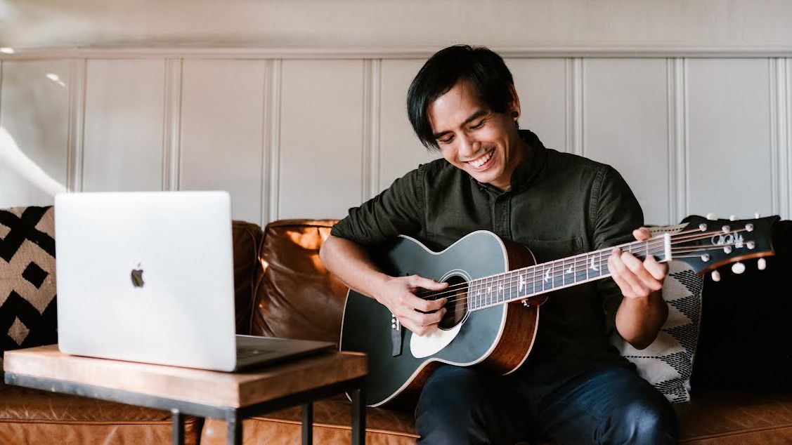 Man playing a PRS acoustic guitar in front of an Apple laptop