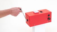A screenshot of a promotional video clip for Squeez Lab's CrankGPT, showing a person's arm rotating a crank attached to a small red box