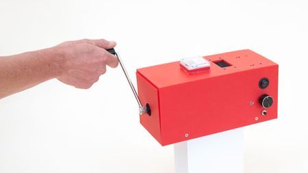 A screenshot of a promotional video clip for Squeez Lab's CrankGPT, showing a person's arm rotating a crank attached to a small red box