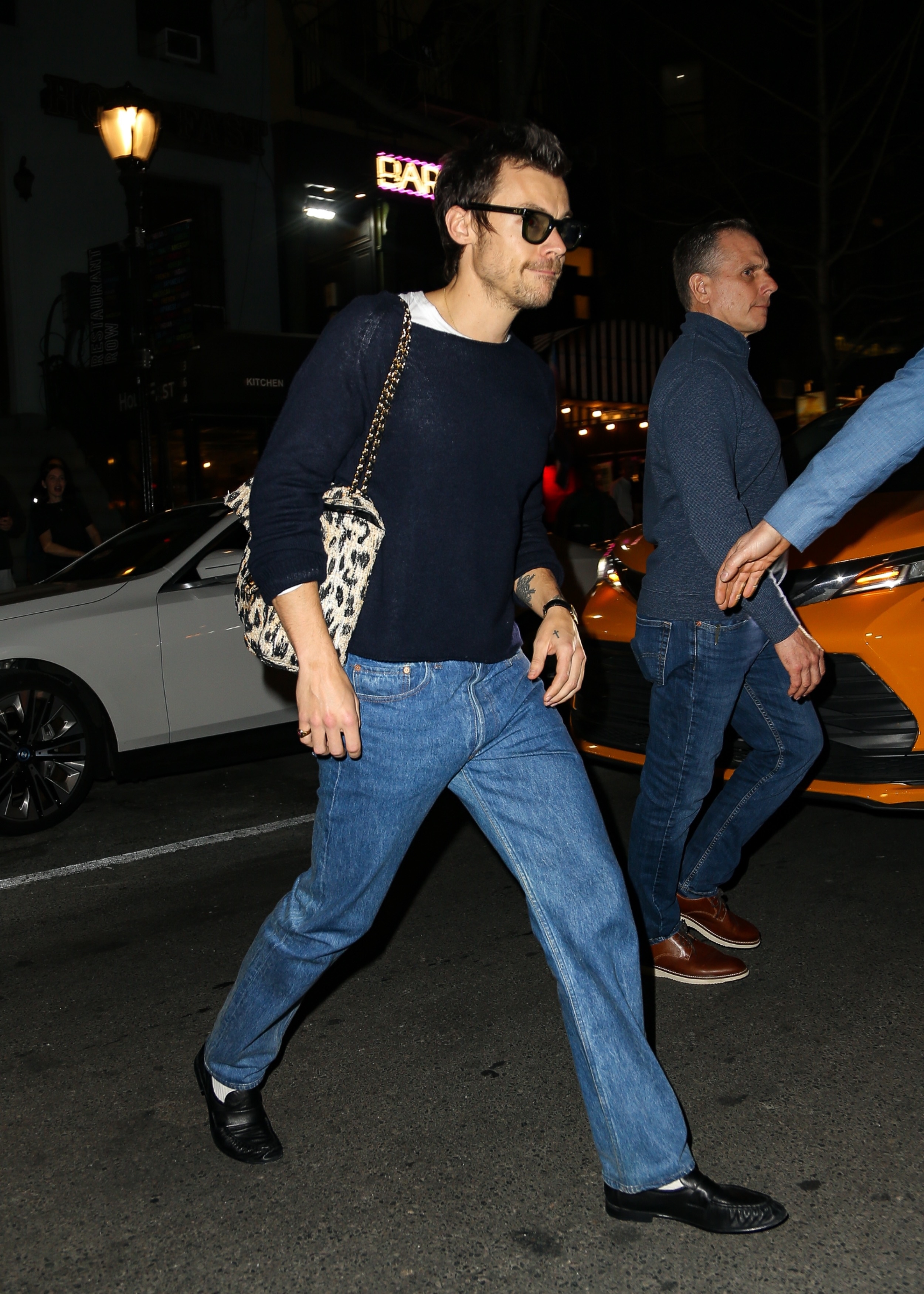 Harry Styles steps out wearing straight-leg jeans with a navy jumper, loafers and a leopard print Chanel bag.