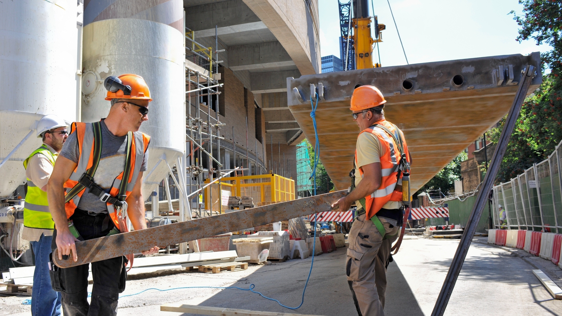 Construction workers lift steel truss on a building site.