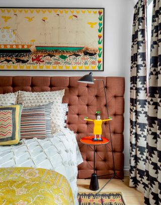bedroom with dark orange headboard, patterned curtains and wall hanging