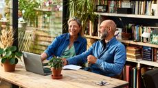 A retired couple sits at home working on a laptop.
