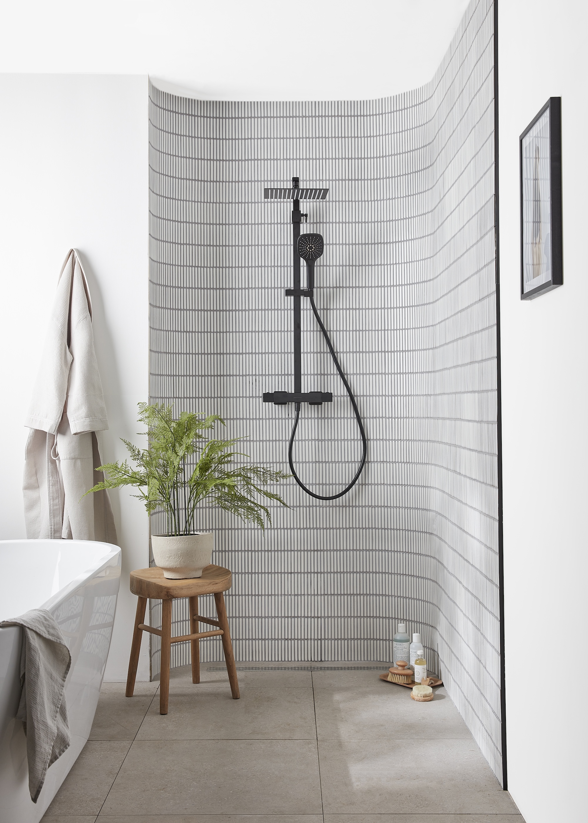 A curved shower with black and white tiles and a side table with a potted plant.