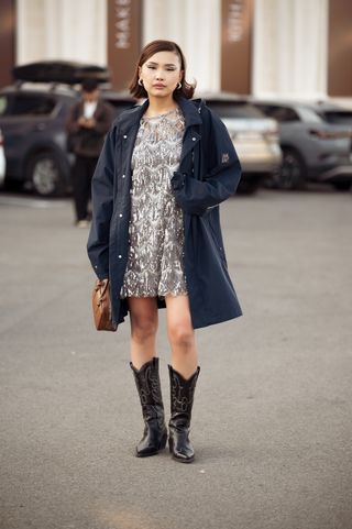 A guest wears silver mini dress, navy blue jacket, brown bag and black cowboy shoes during the 10th season of the Visa Fashion Week Almaty on October 18, 2024 in Almaty, Kazakhstan. (Photo by Raimonda Kulikauskiene/Getty Images)