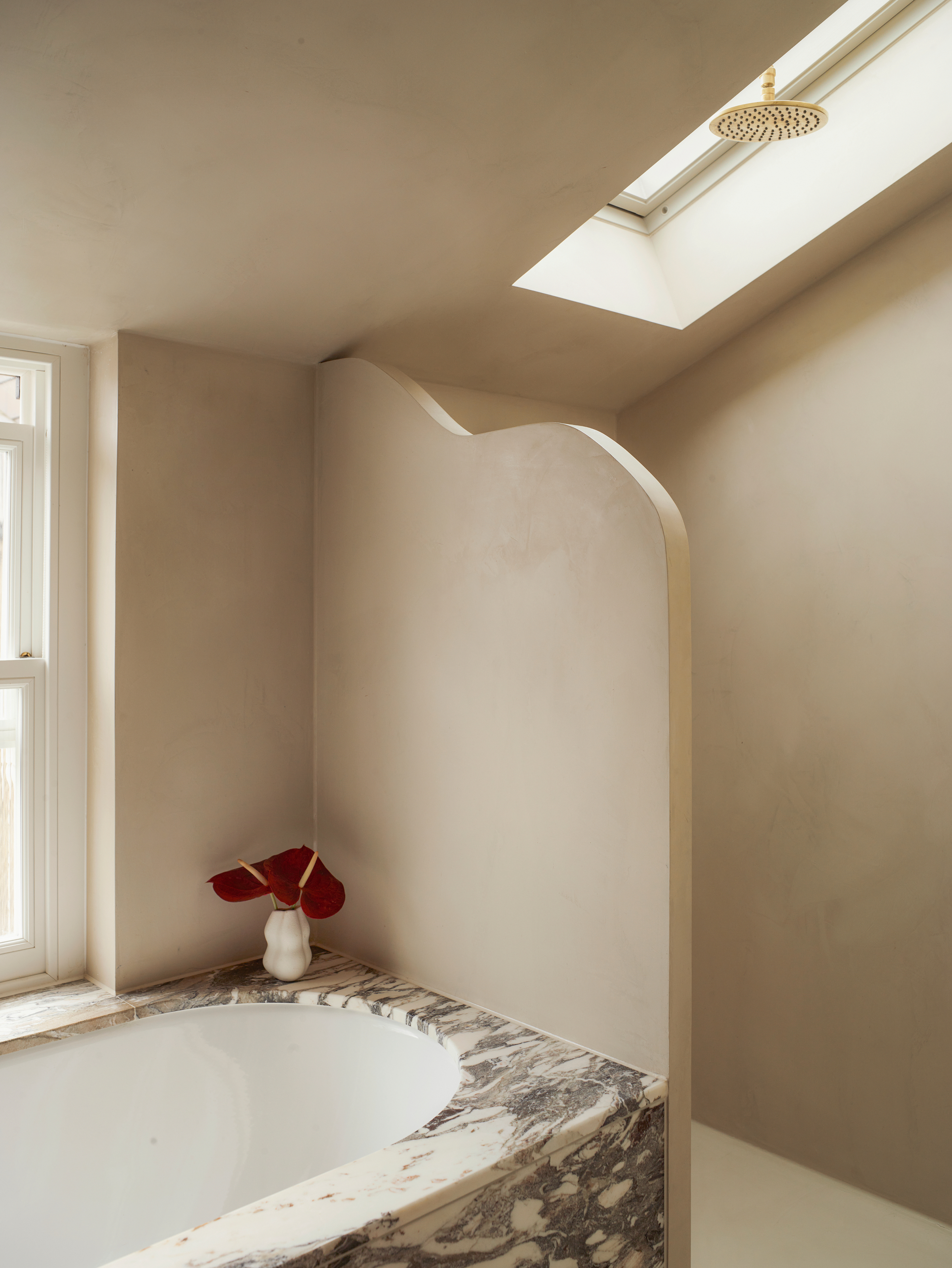Bathroom with limewash beige walls, grey and white marble bath and curved shower divider