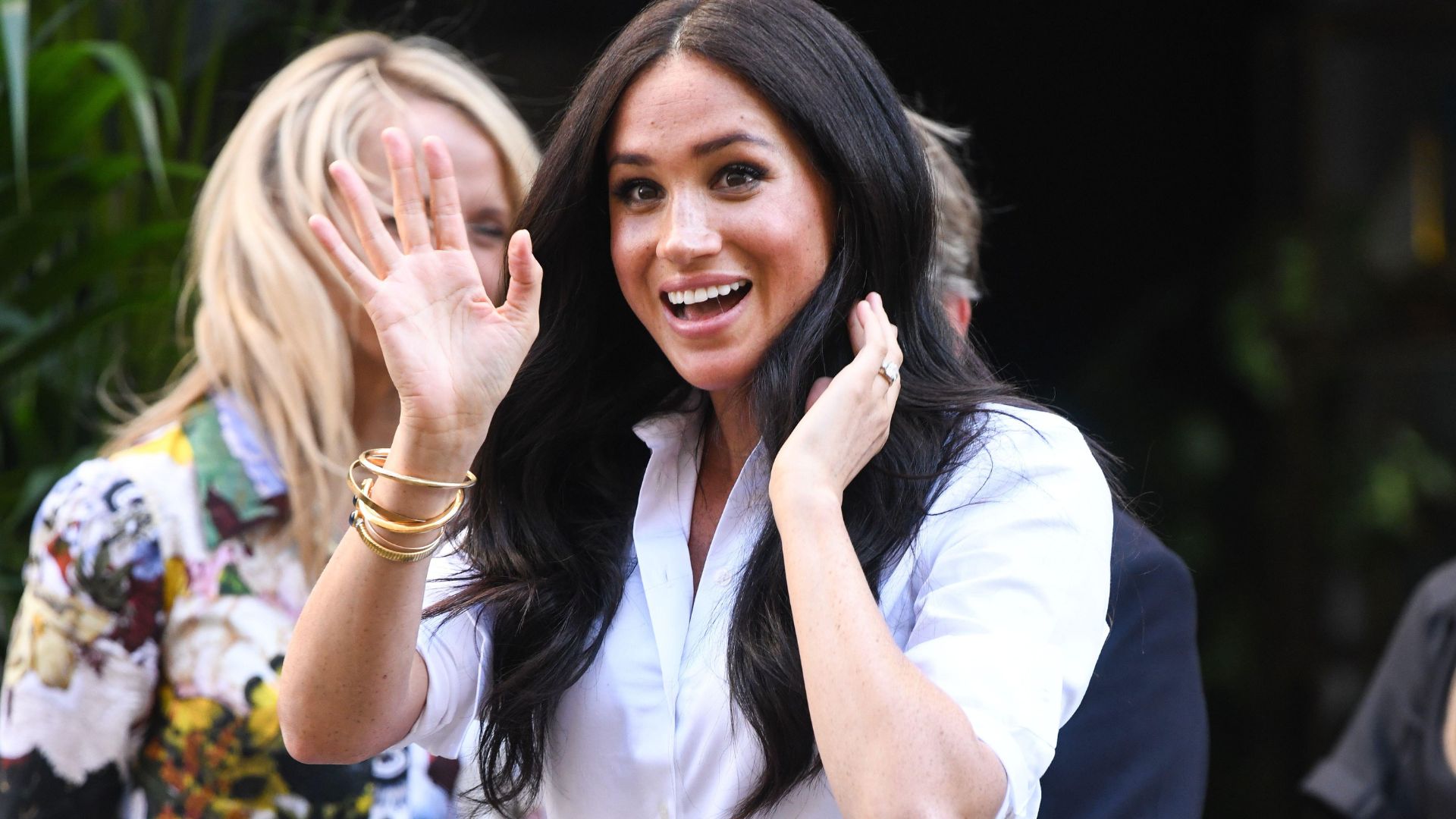Meghan Sussex in a crisp white shirt smiling and waving