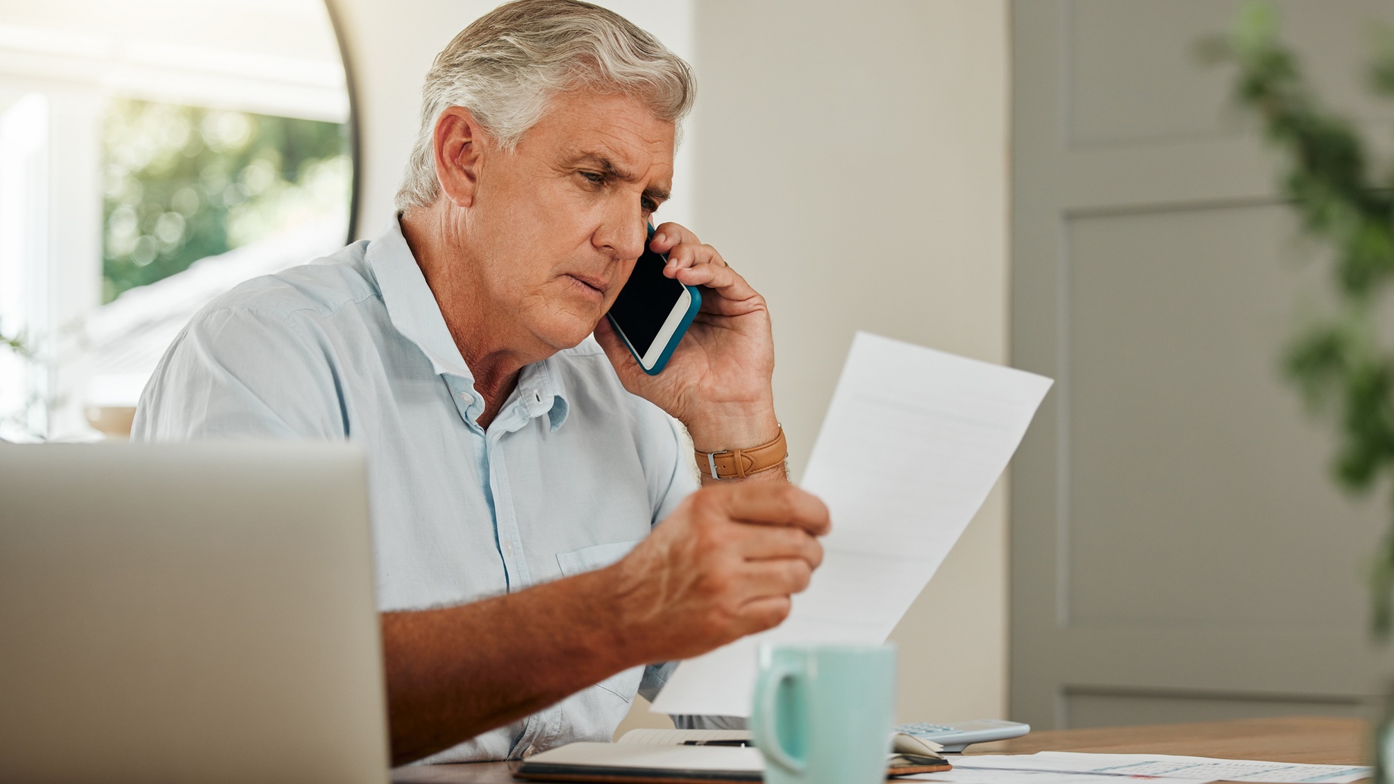 An older man looks at paperwork while talking on the phone.