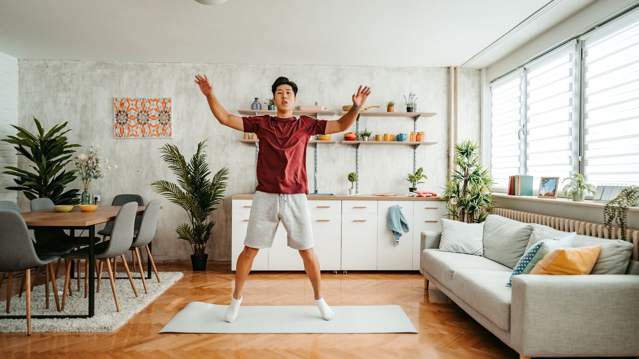 Man doing a star jump on a yoga mat at home