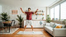 Man doing a star jump on a yoga mat at home