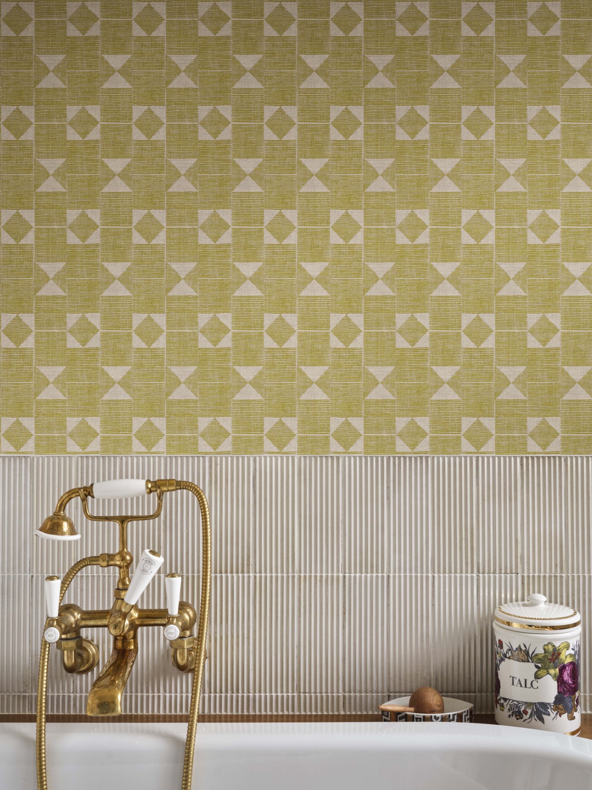 A close-up photograph of a white bath with gold hardware, against a wall papered in yellow, flat-print wallpaper