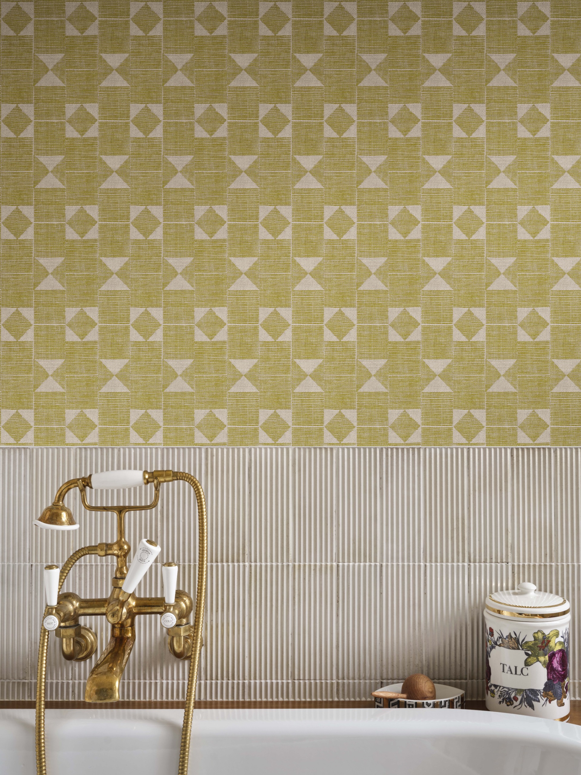 A close-up photograph of a white bath with gold hardware, against a wall papered in yellow, flat-print wallpaper