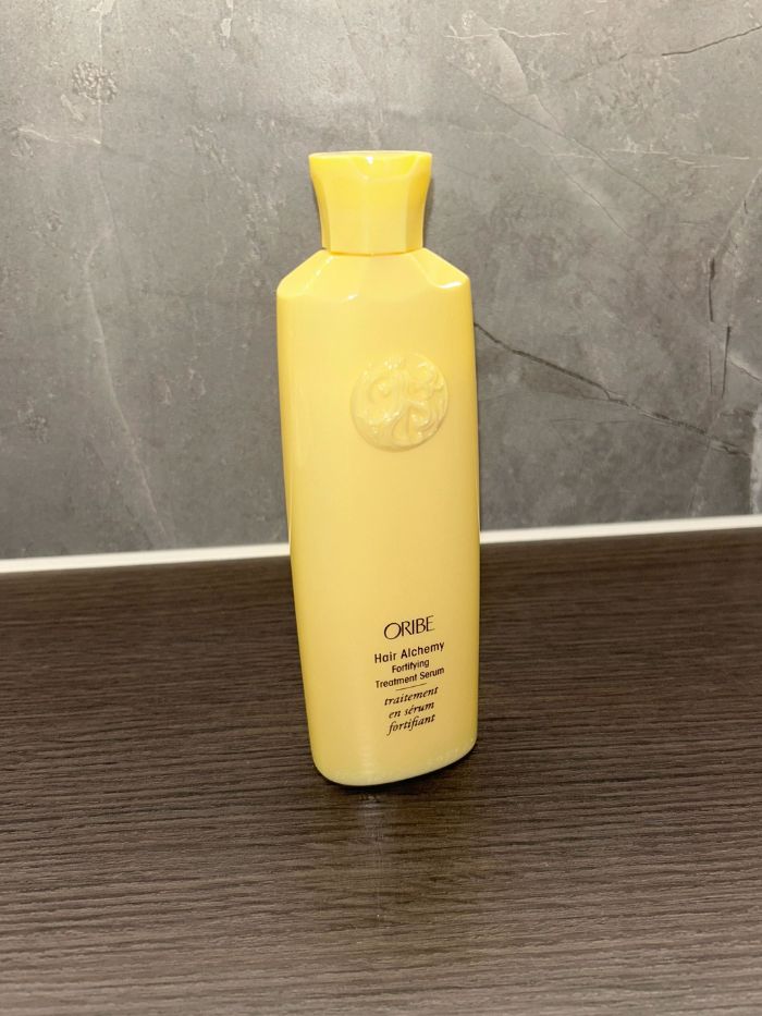 The Oribe Hair Alchemy Fortifying Treatment Serum on the side of a marble bathroom
