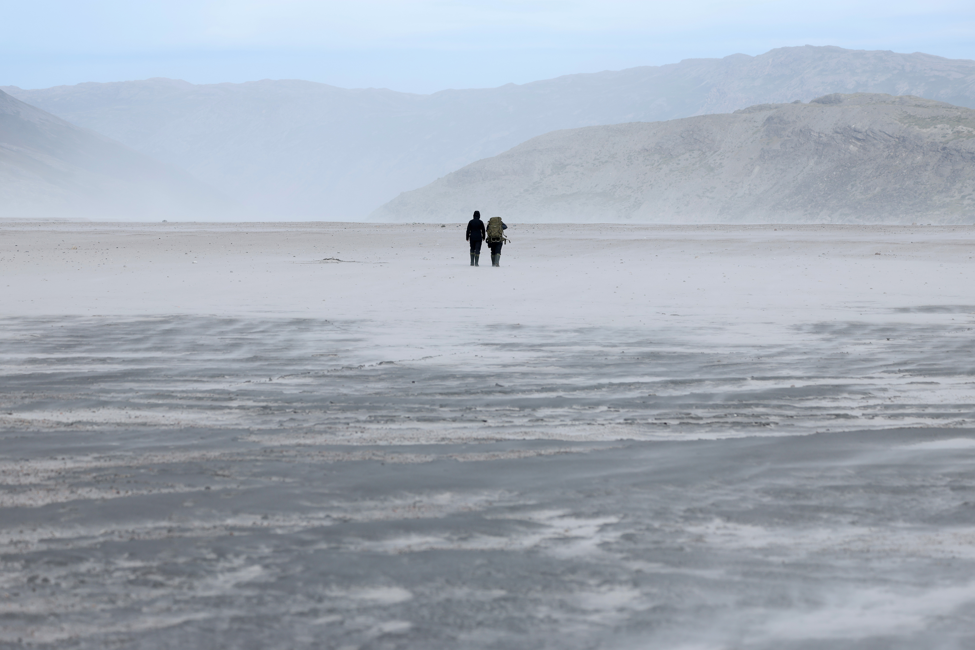 KANGERLUSSUAQ, GREENLAND - JULY 17: Tereza Vosicka (L), a PhD student of hydrobiology in the department of Diatoms in Cryospheric Ecosystems at Charles University in Prague, and Luko P., an undergraduate student in environmental protection at Cryoeco, the Cryosphere Ecology Group at Charles University, walk across a plain of fine sediment left by the Isunnguata Sermia glacier of the Greenland Ice Sheet on July 17, 2026 near Kangerlussuaq, Greenland. A scientific team from Charles University, which is supplying samples and data to other universities internationally, is spending six weeks camped in front of the glacier analyzing the cycle of carbon and organic content emerging in meltwater from the glacier. Bacteria underneath Isunnguata Sermia are consuming organic matter and producing greenhouse gases, including methane, which are released into the atmosphere through meltwater from the ice. The Greenland Ice Sheet is melting at a rate that has accelerated sharply in recent decades. (Photo by Sean Gallup/Getty Images)