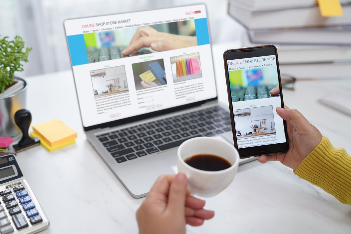 A person using a phone and laptop with a cup of coffee